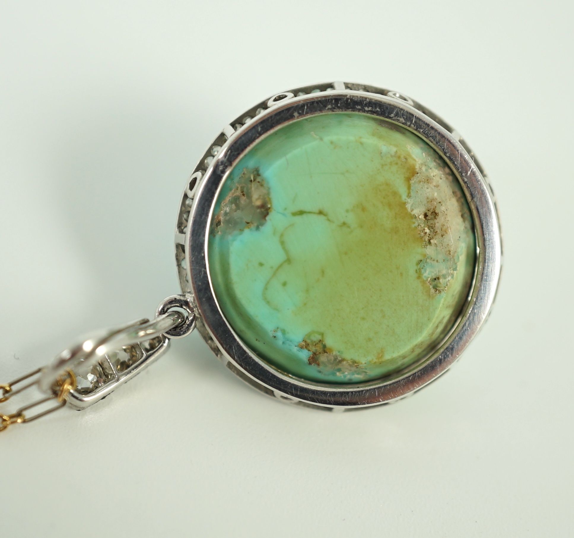 An early 20th century platinum and turquoise set pendant, with diamond chip border and diamond set bale, on a 15ct two colour gold fine link chain